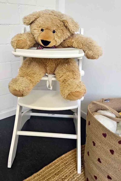 Ein Stofftier (Bär) sitzt in einem Essstuhl für Kinder.