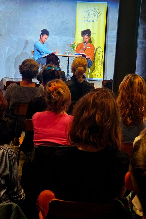 Im Vordergrund sitzt das Publikum der Lesung, im Hintergrund sieht man Fatima Moumouni und Anja Glover, die aus ihrem Buch liest.