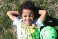 Ein Kind liegt im Gras, daneben ein Ball