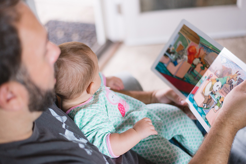 Vater schaut mit Baby ein Buch an.